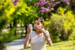 Femme éternuant dans un parc fleuri, allergie aux pollens au printemps